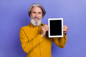 Portrait of attractive cheery gray-haired man showing tablet copy space isolated over bright violet purple color background