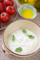 Beige bowl with stracciatella or italian cheese produced from buffalo milk, middle close-up on a beige marble background