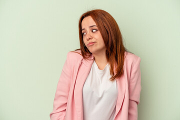 Young caucasian woman isolated on green background shrugs shoulders and open eyes confused.