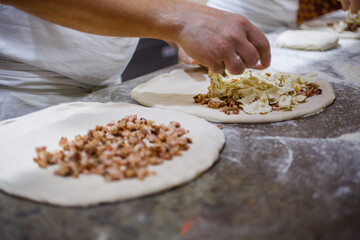 Pizzaiolo mentre prepara due pizze fritte ripiene di mozzarella di bufala e cicoli di maiale