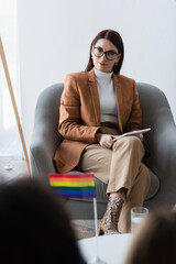 psychologist with digital tablet sitting near patient and lgbt flag on blurred foreground
