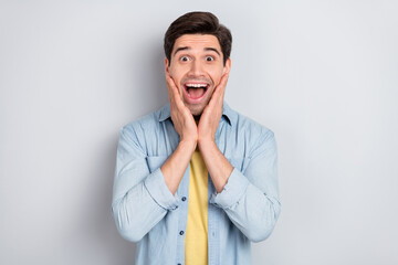 Photo of attractive shocked young guy dressed denim shirt open mouth arms cheeks isolated grey...