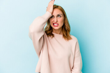 Young caucasian woman isolated on blue background forgetting something, slapping forehead with palm...