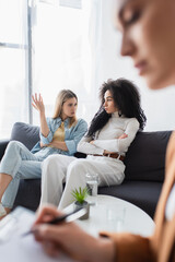 interracial same sex couple quarreling on sofa near blurred psychologist in consulting room