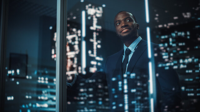 Successful Black Businessman in a Tailored Suit Standing in His Office Looking out of the Window on Night City. Successful Investment Manager Working Late Planning e-Commerce Service Purchase Strategy