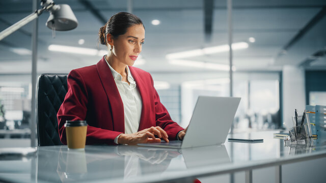 Successful Caucasian Businesswoman in Perfectly Stylish Suit Working on Laptop Computer on Top Floor Office Overlooking Big City. Female CEO Managing Environmental, Social and Corporate Governance - Powered by Adobe