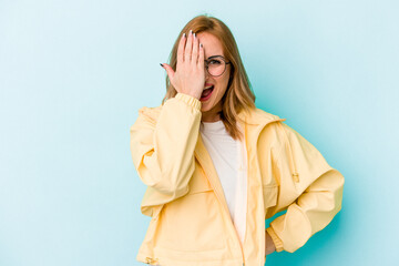 Young caucasian woman isolated on blue background having fun covering half of face with palm.