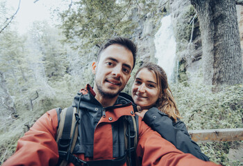 Young caucasian traveler couple taking a selfie near a waterfall.