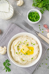 Cauliflower puree with butter and green onions in a white bowl on a gray concrete background. Healthy food. Copy space.