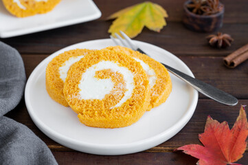 Pumpkin cake roll with cream cheese filling on a dark wooden background. Dessert for Thanksgiving or Halloween. Selective focus, copy space.