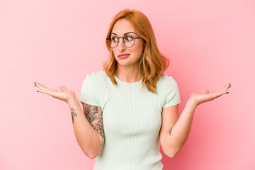 Young caucasian woman isolated on pink background confused and doubtful shrugging shoulders to hold a copy space.