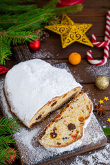 Christmas stollen with dried fruits and powdered sugar on a board on a dark wooden background. Copy space.