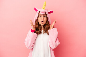 Little caucasian girl wearing a unicorn pajama isolated on pink background surprised and shocked.