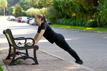 Fototapeta na wymiar a woman in black clothes trains on a park bench . morning sports training for women's health sports lifestyle real life