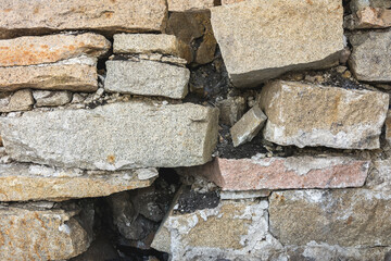 An ancient stone wall made of granite blocks is being destroyed by old age. The texture of natural stone