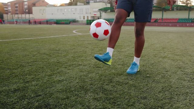 A black soccer player training in a city stadium and juggles a ball on one leg. Close-up. Slow motion