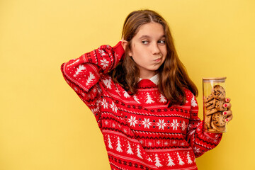Little caucasian girl holding a Christmas cookies isolated on yellow background touching back of head, thinking and making a choice.