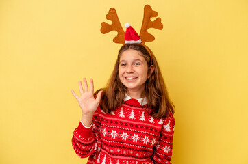 Little caucasian girl wearing a Christmas reindeer hat isolated on yellow background smiling cheerful showing number five with fingers.