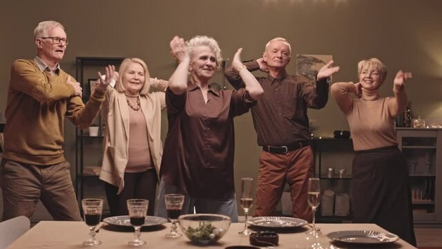 Slowmo shot of five cheerful active seniors having fun while performing Macarena dance at friends home party