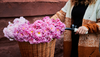 Close up of woman with curly hair and stylish dressed holding bicycle with beautiful bouquet pink...