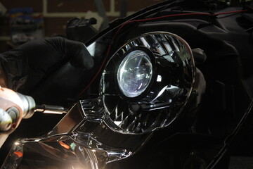 Car headlight in repair close-up. An auto mechanic wearing gloves installs the lens into the...