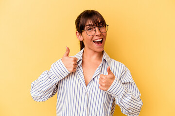 Young Argentinian woman isolated on yellow background raising both thumbs up, smiling and confident.