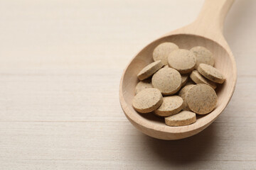 Fototapeta na wymiar Spoon with dietary supplement pills on white wooden table, closeup. Space for text