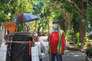 Portrait happy old Asian man street cleaner standing next to an old gabage cart before going to...
