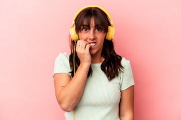 Young Argentinian woman listening to music isolated on pink background biting fingernails, nervous and very anxious.