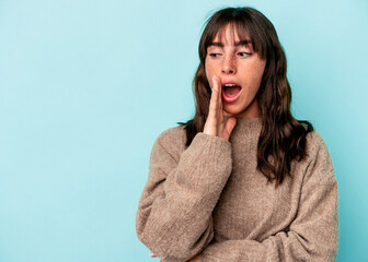 Young Argentinian woman isolated on blue background is saying a secret hot braking news and looking aside