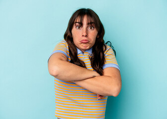 Young Argentinian woman isolated on blue background shrugs shoulders and open eyes confused.