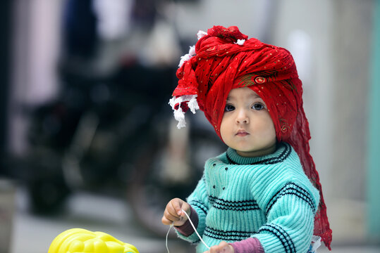 Indian baby girl dressed in green winter sweater and red turban sitting on a toy horse 