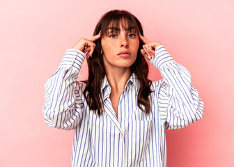 Young Argentinian woman isolated on pink background focused on a task, keeping forefingers pointing head.