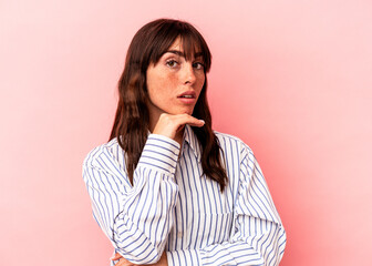 Young Argentinian woman isolated on pink background suspicious, uncertain, examining you.
