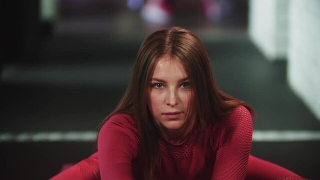 Young pretty woman in red sports suit doing sports in the gym - leaning down with her body sitting down on the splits