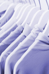 Clothes on hangers and display cases in purple colors of 2022. Turtlenecks, T-shirts, sweaters, sweatshirts in a very peri color.