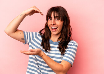Young Argentinian woman isolated on pink background holding something little with forefingers, smiling and confident.