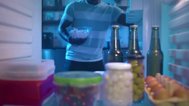 African-American ethnicity man with bowl of popcorn take beer from refrigerator. Realtime