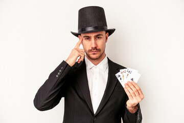 Young caucasian wizard man holding a magic cards isolated on white background pointing temple with finger, thinking, focused on a task.