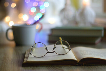 Cup of warm drink with cinnamon stick and candy cane, open book, reading glasses, lit candles and...