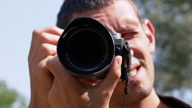 A Photographer Taking Pictures of Nature, Summer Landscape. Smiling, happy unshaved tourist, with a naked body, adjusts the camera, shoots a video on a blurred background of trees in woods. Trip.