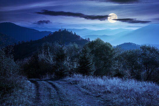mountain scenery in autumn at night. forest in colorful foliage on the hills. distant range beneath a sky with beautiful clouds. wonderful carpathian countryside nature landscape in full moon light