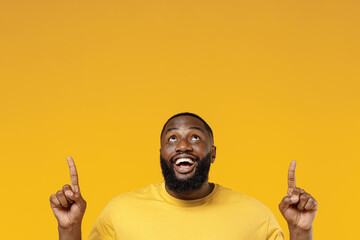 Young smiling happy black man 20s wear bright casual t-shirt point index finger overhead on...