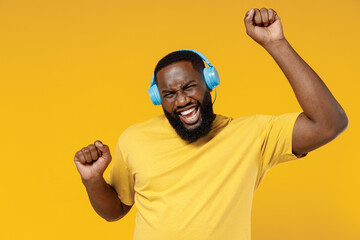 Young smiling excited happy black man 20s wearing bright casual t-shirt headphones listen to music dancing have fun isolated on plain yellow color background studio portrait. People lifestyle concept.