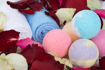 a set of multicolored balls of colored sea salt, surrounded by rose petals and towels, for taking a bath, close-up