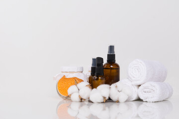 Obraz na płótnie Canvas on a white background, rolled towels, aromatic oils for massage and yellow bath salt in a glass jar, there is a place for the inscription