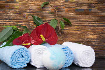 Obraz na płótnie Canvas on a dark wooden background, towels for spa treatments wrapped in a roll, a ball of salt and a flower