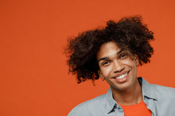 Close up young smiling happy cheerful satisfied friendly positive black student man 50s wear blue shirt t-shirt look camera isolated on plain orange color background studio. People lifestyle concept.