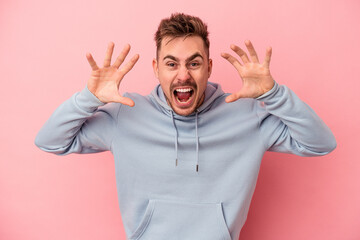 Young caucasian man isolated on pink background showing claws imitating a cat, aggressive gesture.