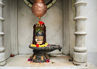 A Close up picture of a Shiva Lingam made of stone material with a brass vessel to anoint milk to...